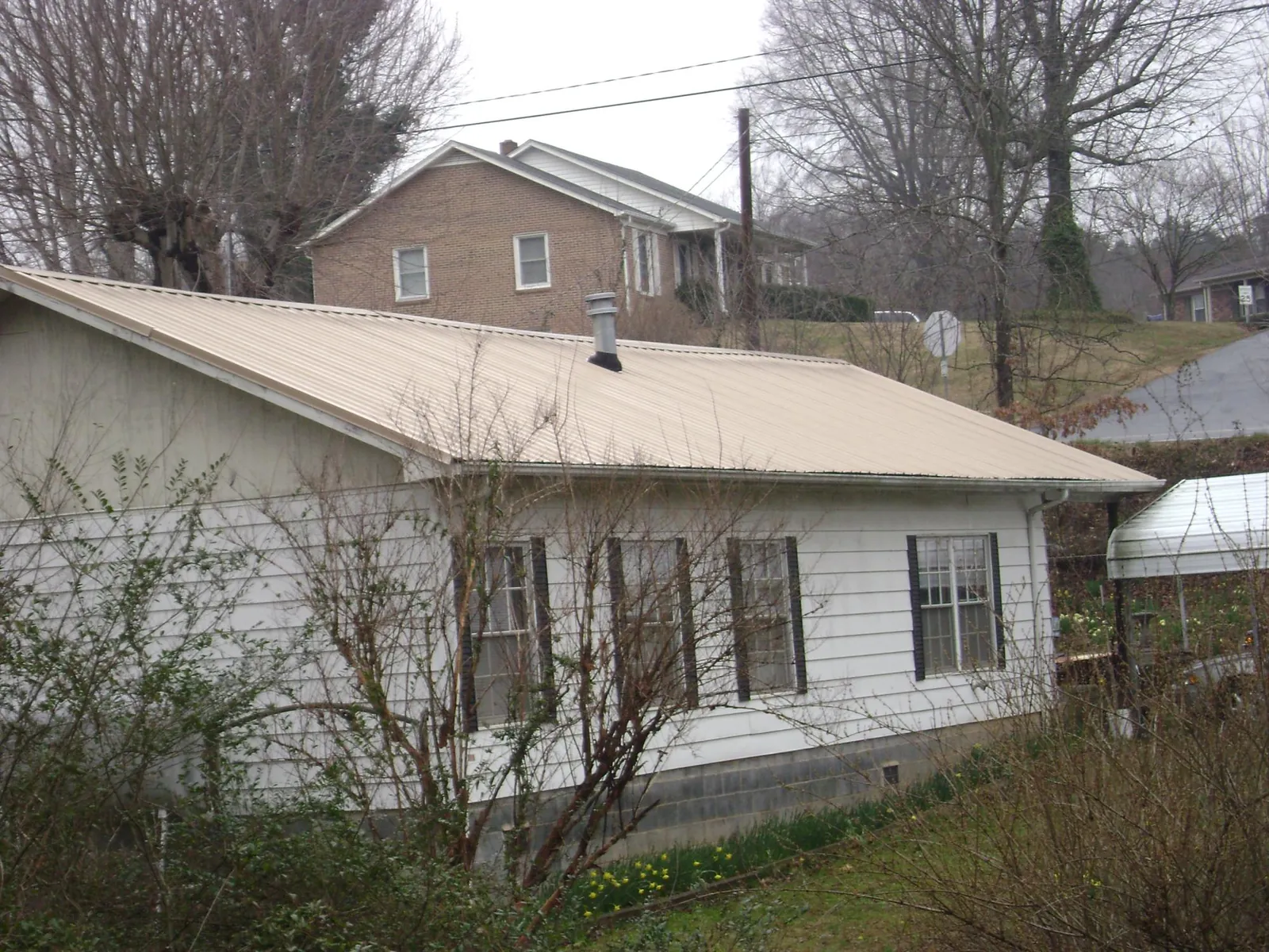Tan metal roof on a white sided house set into a hillside — Commercial Roofing by Roofing Brothers in Butler